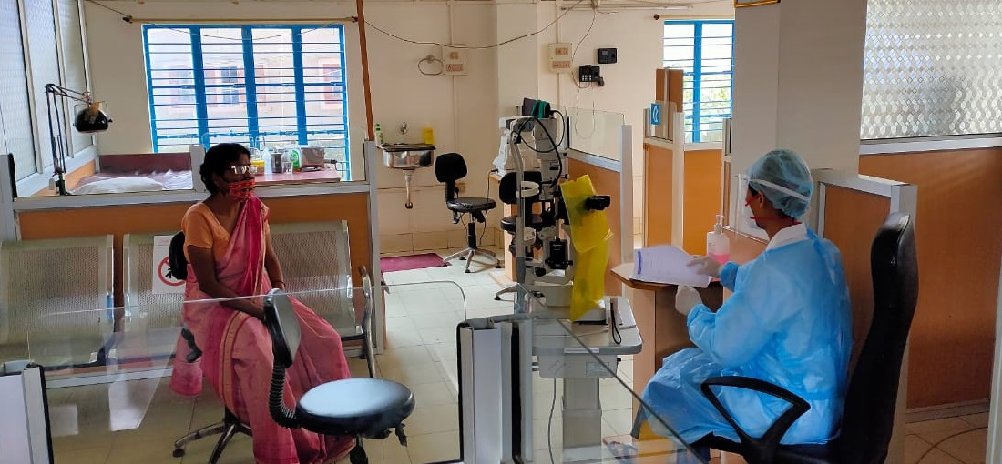 A medical professional wearing blue PPE along with a patient in an eye clinic